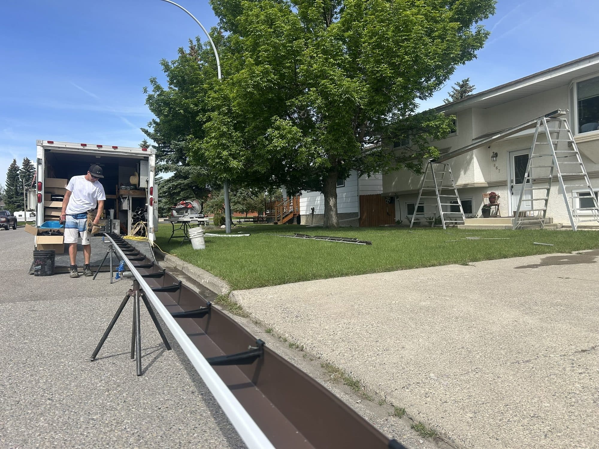 A crew member running a length of seamless eavestrough off the forming machine in the trailer, on-site at a customer's home