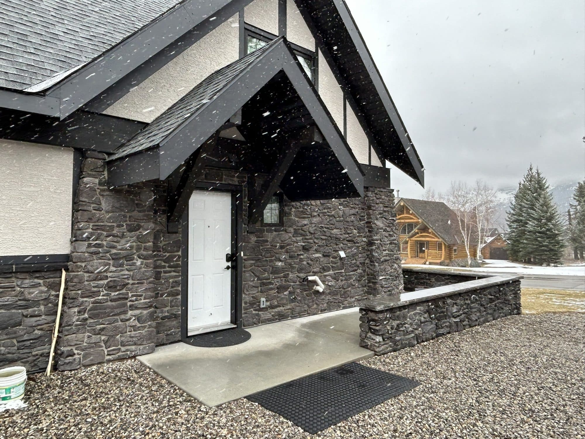 A stone-clad entry and knee wall built by First Class Stucco & Masonry on a Tudor-style new build